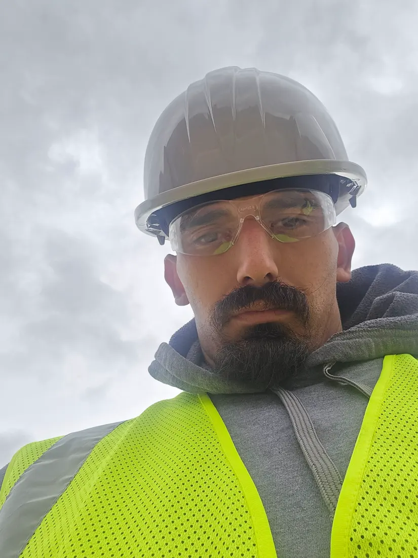 Michael Flores in a hard hat, safety glasses, and hi-vis vest on a job site